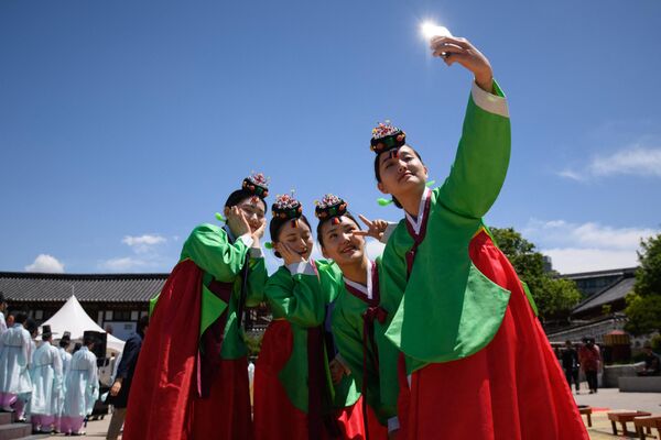 Молодые женщины в традиционных платьях ханбок делают селфи после традиционной церемонии по случаю Дня совершеннолетия в деревне  Намсан ханок в Сеуле, Южная Корея. - Sputnik Узбекистан