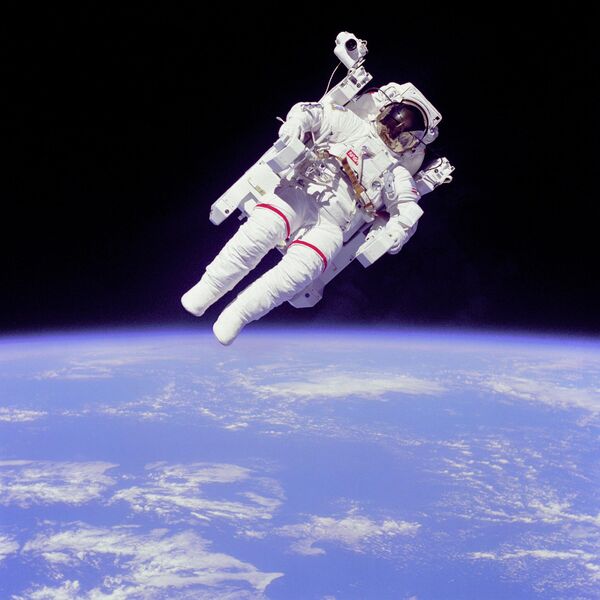 Астронавт Брюс МакКендлс в открытом космосе в нескольких метрах от космическогого шаттла Челленджер. Астронавт не пристегнут к кабине аппарата. В свободном полете он передвигается с помощью портативного двигателя. На заднем фоне можно увидеть Землю. - Sputnik Узбекистан