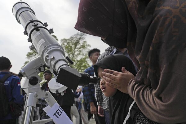 Женщина помогает дочери увидеть в телескоп солнечное затмение в Джакарте, Индонезия.  - Sputnik Узбекистан