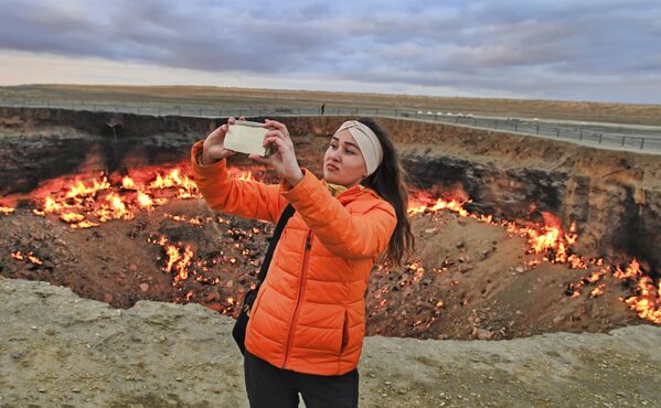 Девушка делает селфи на фоне горящего кратера &quot;Врата ада&quot;, пустыня Каракумы в Туркменистане.  - Sputnik Узбекистан