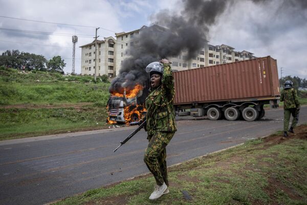 Женщина-омоновец просит подкрепление после того, как сторонники оппозиции подожгли грузовик в Кении.  - Sputnik Узбекистан