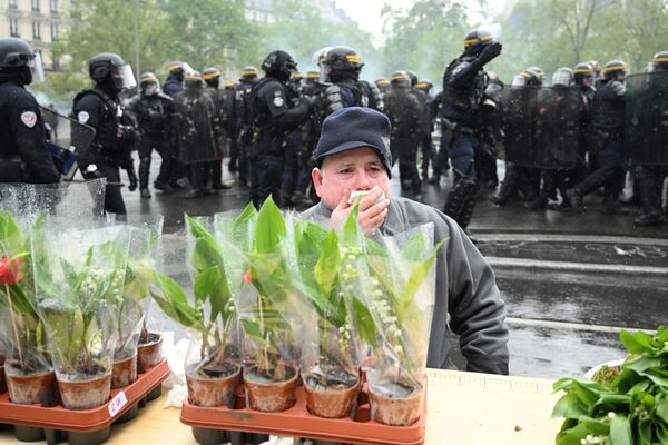 Уличный торговец, продающий веточки ландыша прикрывает нос от слезоточивого газа, который выпустила полиция во Франции.  - Sputnik Узбекистан