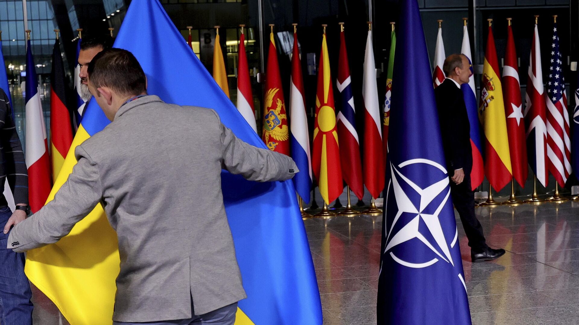 Сотрудник службы протокола поправляет украинский флаг в штаб-квартире НАТО в Брюсселе 7 апреля 2022 года.  - Sputnik Узбекистан, 1920, 16.06.2023