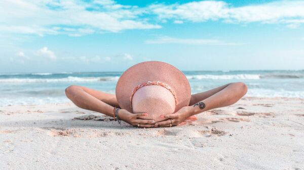 Женщина в коричневой шляпе лежит на песке. - Sputnik Узбекистан