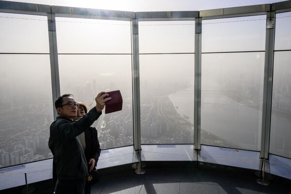 Те, кто могут себе позволить, спасаются в зданиях с системой кондиционирования и очистки воздуха. Туристы фотографируются на фоне города, укрытого пыльным воздухом, Сеул, апрель 2023 года. - Sputnik Узбекистан