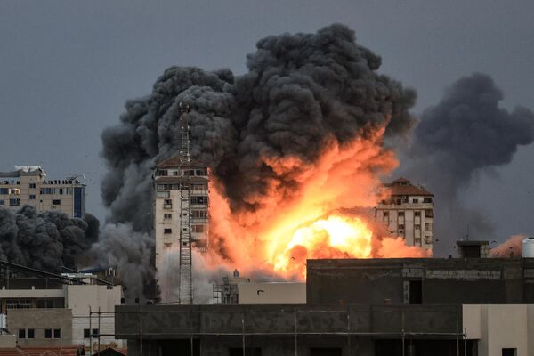Люди, стоящие на крыше, наблюдают, как шар огня и дыма поднимается над зданием в городе Газа 7 октября 2023 года, во время авиаудара Израиля по зданию Палестинской башни.  - Sputnik Узбекистан