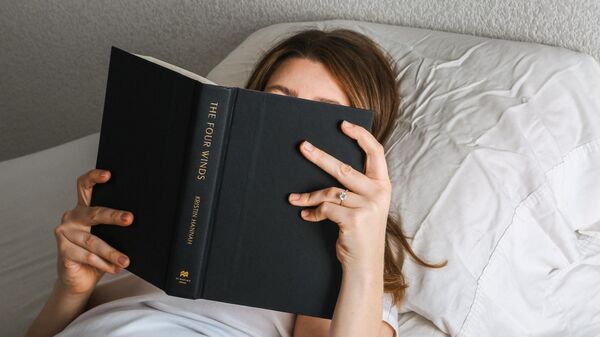Девушка читает книгу лежа на кровати. - Sputnik Узбекистан