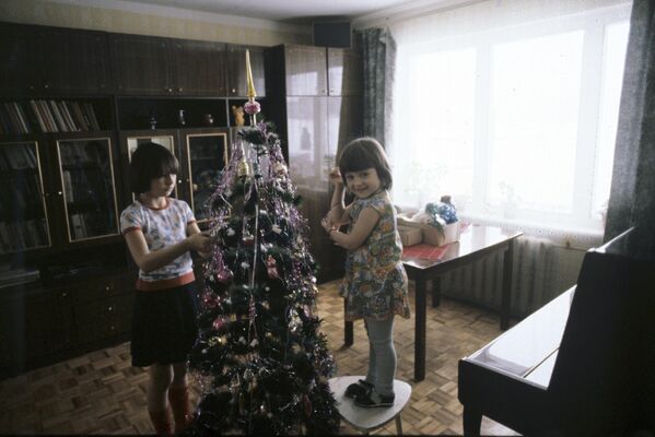 1983 год. Маленькие жители поселка Вельяминово Московской области  наряжают новогоднюю елку. Игрушки бережно хранили весь год в коробке, переложенные газетами и ватой. Макушку елки обычно украшали стеклянной верхушкой или пятиконечной звездой - Sputnik Узбекистан