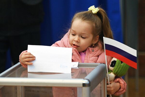 Девочка опускает в избирательную урну бюллетень на избирательном участке в посольстве РФ в Минске - Sputnik Узбекистан