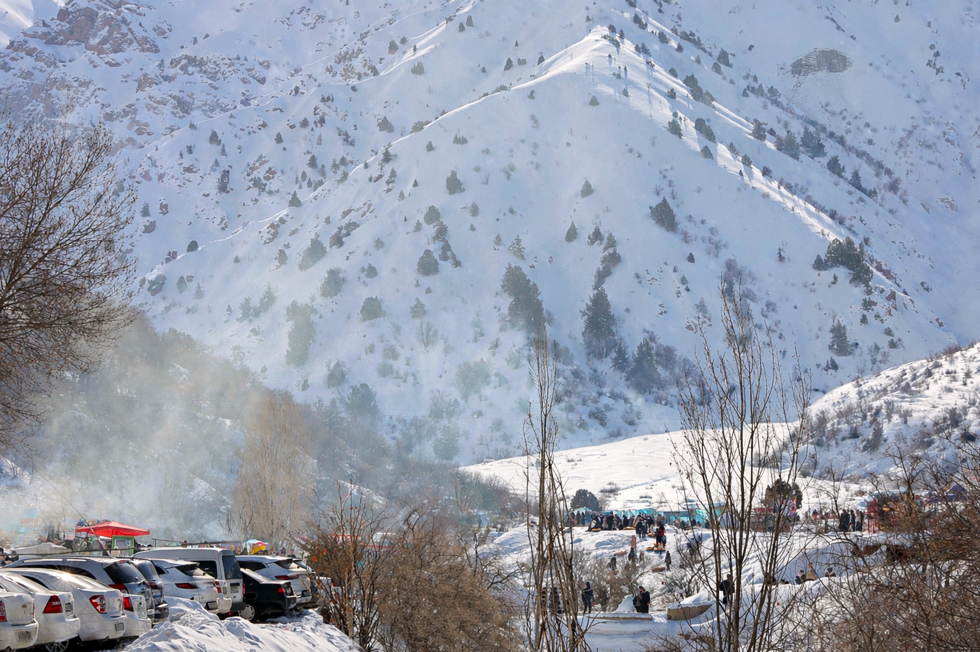 Қорли Чимён тизмаларининг қишки гўзаллиги. Фотосуратда оппоқ қор билан бурканган тоғ ён бағирлари ва унинг пойидаги машиналар билан тўлган гавжум тўхташ жойи акс этган. - Sputnik Ўзбекистон, 1920, 12.02.2026