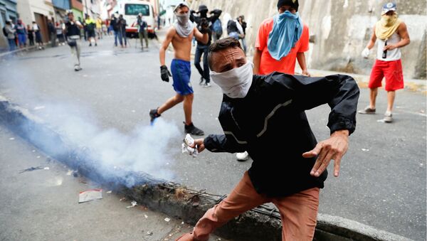 Демонстрант бросает обратно канистру со слезоточивым газом во время столкновения с Национальной гвардией Венесуэлы  - Sputnik Ўзбекистон