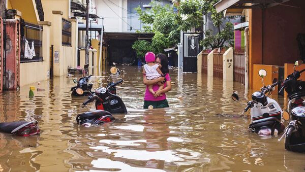 Женщина несет на руках ребенка по затопленной улице индонезийского города  - Sputnik Узбекистан