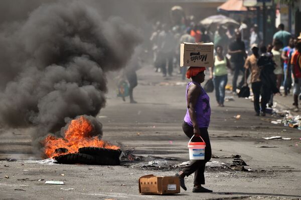 Женщина проходит мимо горящей шины на улице Порт-о-Пренса, столицы Гаити - Sputnik Узбекистан