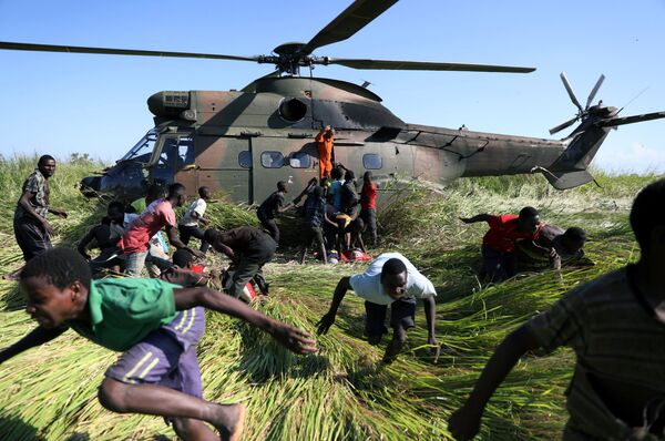 Местные жители разбегаются от вертолета Южно-Африканских национальных сил обороны, который привез продовольственную помощь в деревню, пострадавшую от циклона, Мозамбик - Sputnik Узбекистан