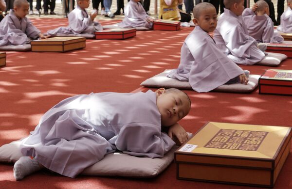 Мальчик дремлет после церемонии бритья головы и посвящения в монахи по случаю предстоящего 2563-го дня рождения Будды в храме Джогье в Сеуле, Южная Корея - Sputnik Узбекистан