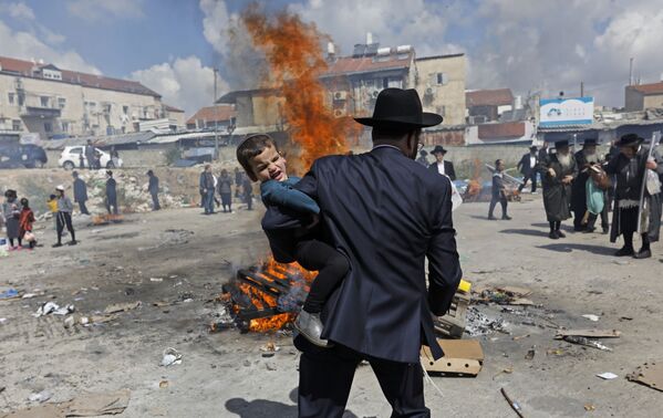 Ультраортодоксальный еврейский мужчина несет ребенка во время ритуала Биур Хамец в Иерусалиме, в канун еврейского праздника Песах (Пасха) - Sputnik Узбекистан