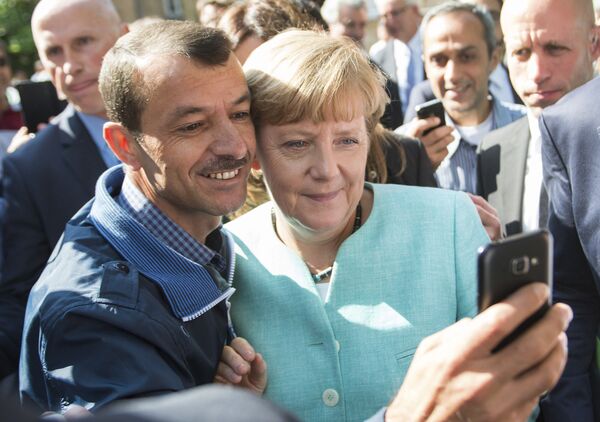 Беженец делает селфи с канцлером Германии Ангелой Меркель во время ее визита в центр для новоприбывших беженцев в Берлине - Sputnik Узбекистан