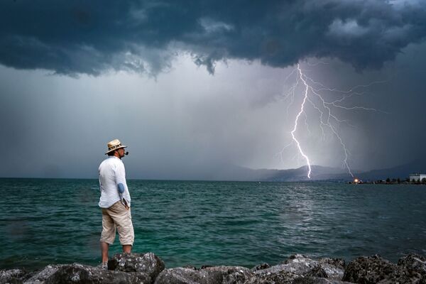 Мужчина на фоне молнии на горизонте озера Женева в Швейцарии - Sputnik Узбекистан