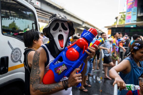 Человек в маске и с водяным пистолетом во время празднования буддийского нового года в Бангкоке - Sputnik Узбекистан