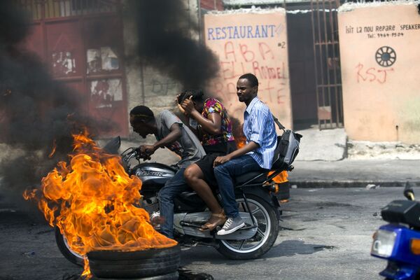 Мототакси, проезжающее мимо горящей шины в Порт-о-Пренсе, Гаити - Sputnik Узбекистан