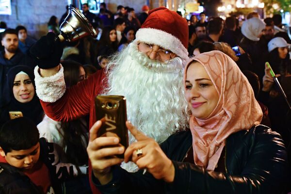 Женщина фотографируется с мужчиной в костюме Санта-Клауса на праздновании Рождества в сирийской Латакии - Sputnik Узбекистан