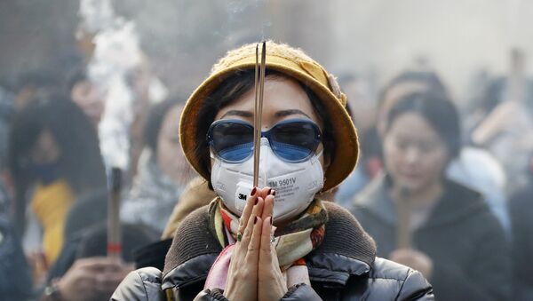 Jenshina v maske i solnsezashitnix ochkax vo vremya molitvi v perviy den Novogo goda v Pekine - Sputnik O‘zbekiston