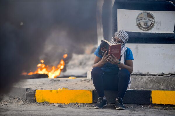 Участник антипровительственных протестов читает роман на фоне горящих шин, Эн-Наджаф, Ирак - Sputnik Узбекистан