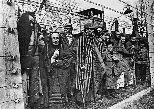 Заключенные концлагеря Освенцим смотрят в объектив из-за колючей проволоки - Sputnik Узбекистан