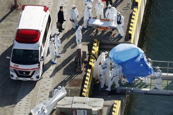 Сотрудники полиции в защитных костюмах помещают в машину скорой помощи заболевшего пассажира круизного лайнера Diamond Princes, помещенного в карантин у японского порта Йокогама - Sputnik Узбекистан
