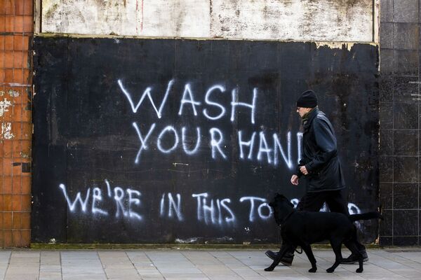 Мужчина с собакой напротив граффити с призывом мыть руки в Северной Ирландии - Sputnik Узбекистан