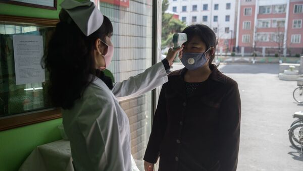 Медицинский работник измеряет температуру посетительнице в медицинской маске на входе в больницу в Пхеньяне, Северная Корея - Sputnik Ўзбекистон