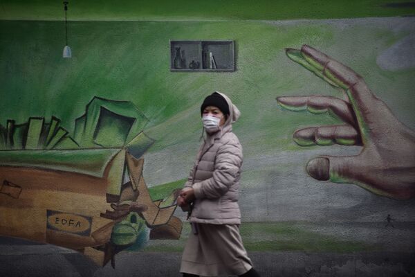 Местная жительница в Ухане, Китай, проходит на фоне стены с граффити - Sputnik Узбекистан