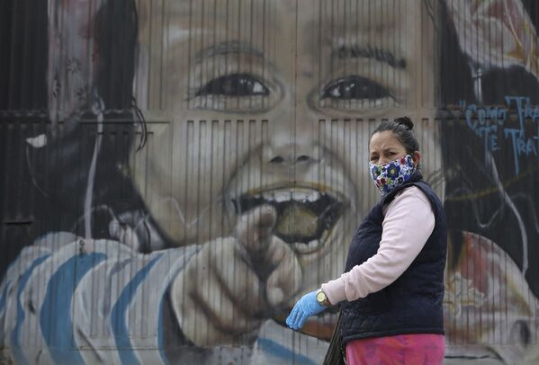 Женщина в защитной маске и перчатках проходит мимо настенной росписи в Соача на окраине Боготы, Колумбия - Sputnik Узбекистан