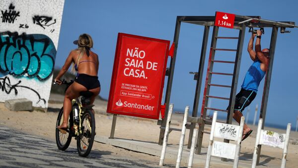 Девушка на велосипеде проезжает мимо плаката «Не выходи из дома» на пляже Ipanema в Рио-де-Жанейро, Бразилия - Sputnik Ўзбекистон