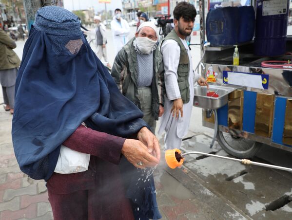 Сотрудники афганской национальной службы закупок распыляют дезинфицирующее средство на руки женщины - Sputnik Ўзбекистон