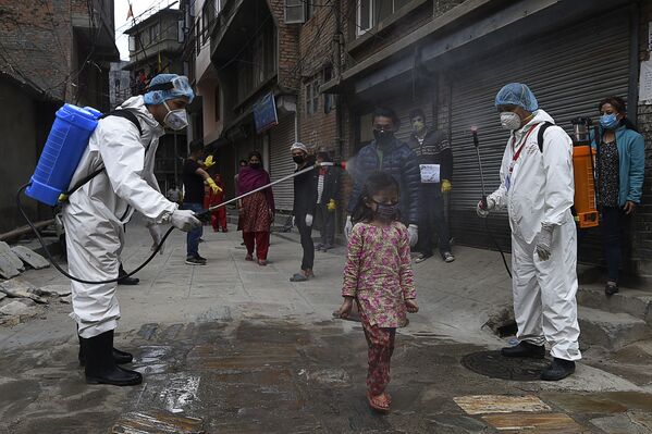 Медицинские работники в защитных костюмах распыляют дезинфицирующее средство на девочку в Катманду, Непал - Sputnik Узбекистан
