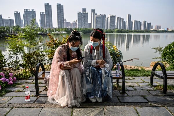 Молодые женщины в масках и в традиционных костюмах на скамейке в парке Уханя, Китай. - Sputnik Узбекистан