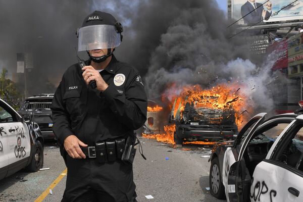 Полицейский Лос-Анджелеса на фоне горящей машины во время протестов  - Sputnik Узбекистан