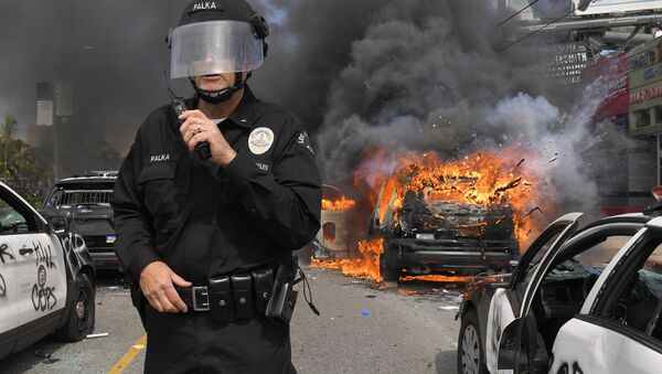 Полицейский Лос-Анджелеса на фоне горящей машины во время протестов  - Sputnik Ўзбекистон