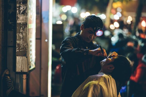 Барбер бреет клиента при свете фонаря на улице Ханоя, Вьетнам - Sputnik Ўзбекистон