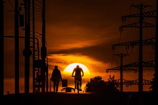 Мужчина едет на велосипеде по одной из московских улиц на фоне заката. - Sputnik Узбекистан