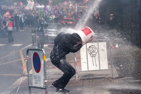 Протестующий прикрывается ведром от удара водяной пушкой, которую полицейские используют для разгона акции протеста медработников в Нанте, Франция. - Sputnik Узбекистан