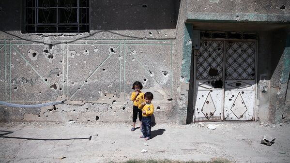 Дети стоят напротив стены, изрешеченной пулями в пригороде Дамаска - Sputnik Узбекистан
