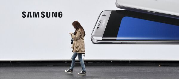Женщина проходит мимо стенда с изображением телефона Samsung Женщина проходит мимо стенда с изображением телефона Samsung - Sputnik Узбекистан
