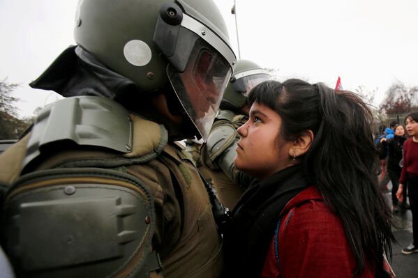 Девушка смотрит на полицейского во время беспорядков в Чили - Sputnik Узбекистан