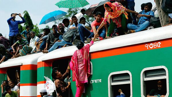 A woman helps another woman to get atop of an overcrowded passenger train as they travel home to celebrate Eid al-Fitr festival at a railway station in Dhaka - Sputnik Узбекистан