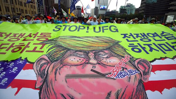 South Korean protesters carry a banner showing a caricature of US President Donald Trump as they march towards the US embassy during an anti-US rally demanding peace in the Korean Peninsula in Seoul on August 15, 2017. North Korean leader Kim Jong-Un said on August 15 he would hold off on a planned missile strike near Guam, but warned the highly provocative move would go ahead in the event of further reckless actions by Washington. - Sputnik Узбекистан