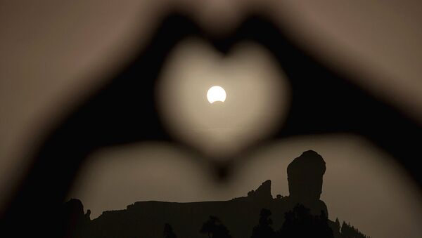 A woman makes a heart shape with her hands during a partial eclipse of the sun over the Roque Nublo mountain at the Canary Island of Gran Canaria - Sputnik Узбекистан