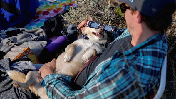 An enthusiast holds his dog Prince, who sports solar glasses, as they await a total solar eclipse from atop Carroll Rim Trail at Painted Hills, a unit of the John Day Fossil Beds National Monument, near Mitchell, Oregon, U.S - Sputnik Узбекистан