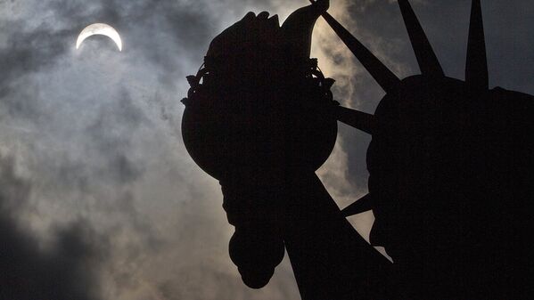 A partial solar eclipse appears over the Statue of Liberty on Liberty Island in New York, Monday - Sputnik Узбекистан